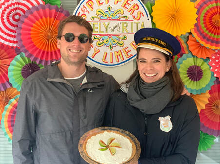 Young Atlanta couple smiles in front of colorful backdrop at Atlanta's pie festival. Women holds a delicious key lime pie.